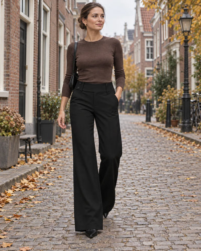 Vrouw in een zwarte wijde broek met hoge taille en een bruine top wandelt door een herfstige straat